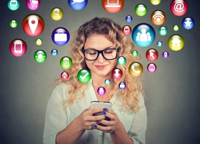 Photo of a young lady working on her phone with social media icon bubbles floating out of the phont